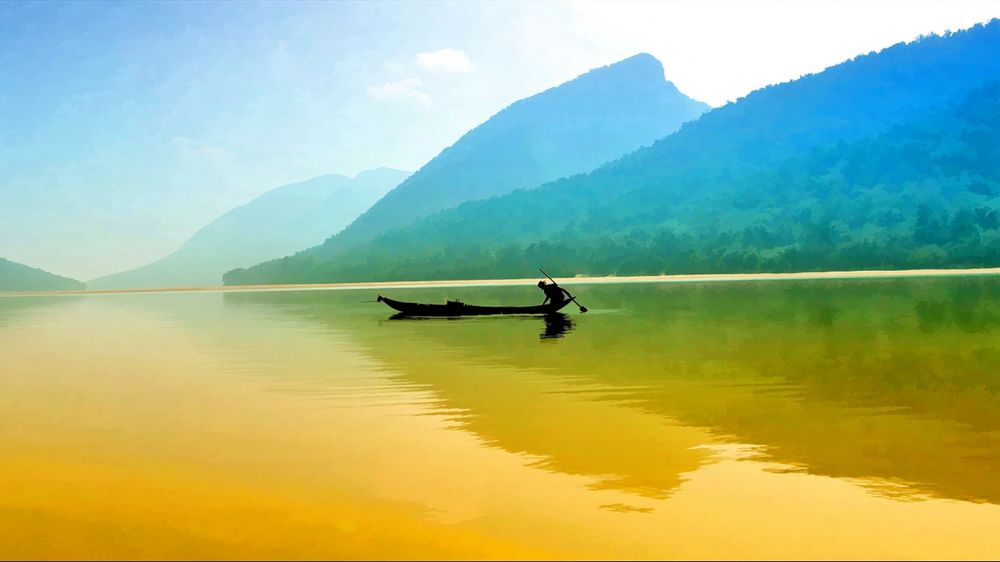 Обои для рабочего стола Мужчина плывет в лодке по водной глади озера, в котором отражаются лес, горы и небо
