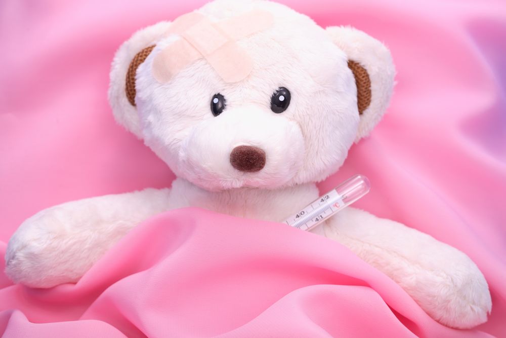 Обои для рабочего стола Белый плюшевый медведь лежит под розовым покрывалом с градусником, голова заклеена лейкопластырем
