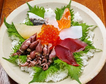Обои на рабочий стол Японская кухня: кальмары, икра и ломтики разной рыба с рисом на белом блюде