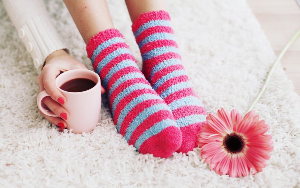 Обои для рабочего стола Ножки девушки в полосатых носочках и рука с кружкой кофе на мягком коврике, рядом лежит розовая гербера
