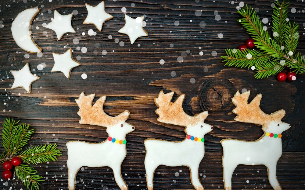 Обои для рабочего стола Рождественское печенье в виде оленей, звезд и месяца лежат на деревянной поверхности возле еловых веточек