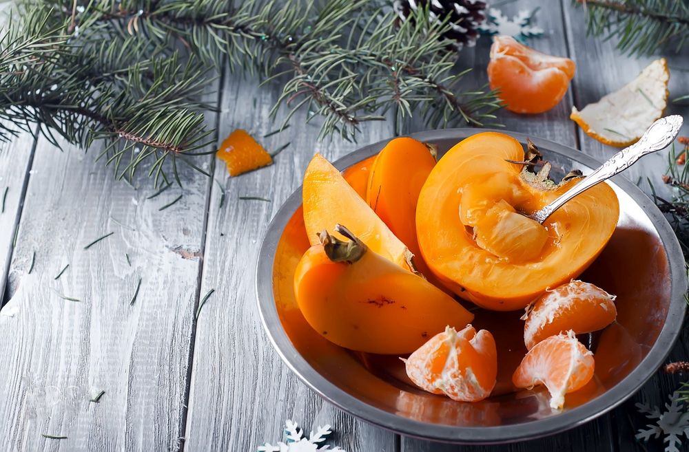 Обои для рабочего стола Свежие фрукты хурма и мандарины на деревянном столе с рождественскими украшениями, фотограф Yuliia Мазуркевич