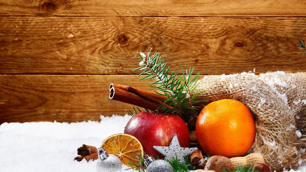Обои для рабочего стола Апельсин, красное яблоко и пряности лежат на снегу с еловыми ветками