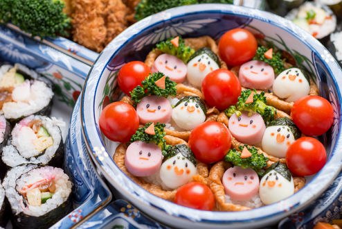 Обои на рабочий стол Японская кухня: миска с помидорами, яйцами и кусочками колбасы с рожицами, рядом роллы и зелень