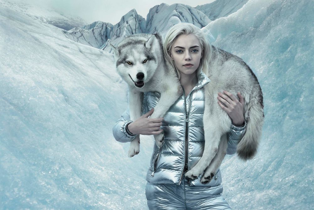 Обои для рабочего стола Девушка блондинка держит на шее собаку хаски на фоне зимних гор, by Annie Leibovitz