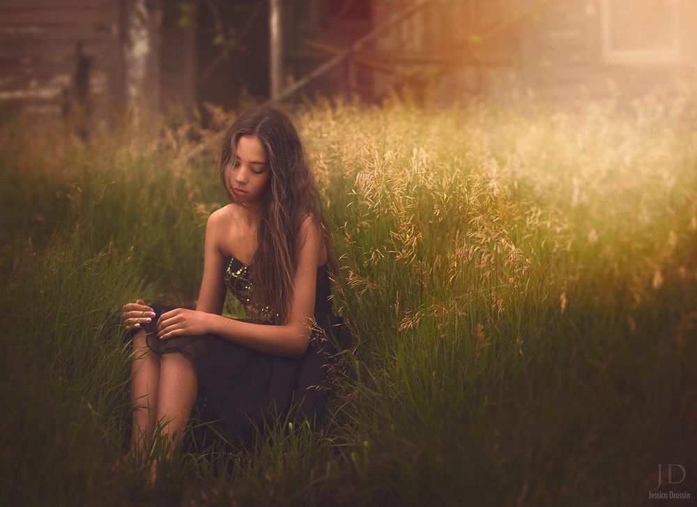 Обои для рабочего стола Девушка грустно склонив голову сидит на лугу в траве, положив руки на колени на фоне закатного вечера, by Djessica Drossin