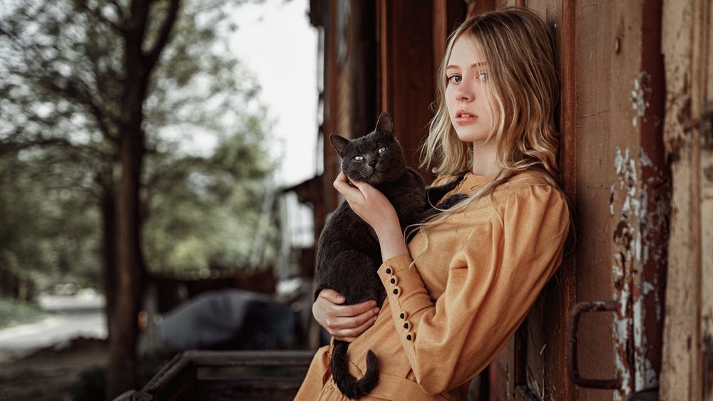 Обои для рабочего стола Девушка с котом на руках стоит у стены дома, фотограф Георгий Чернядьев