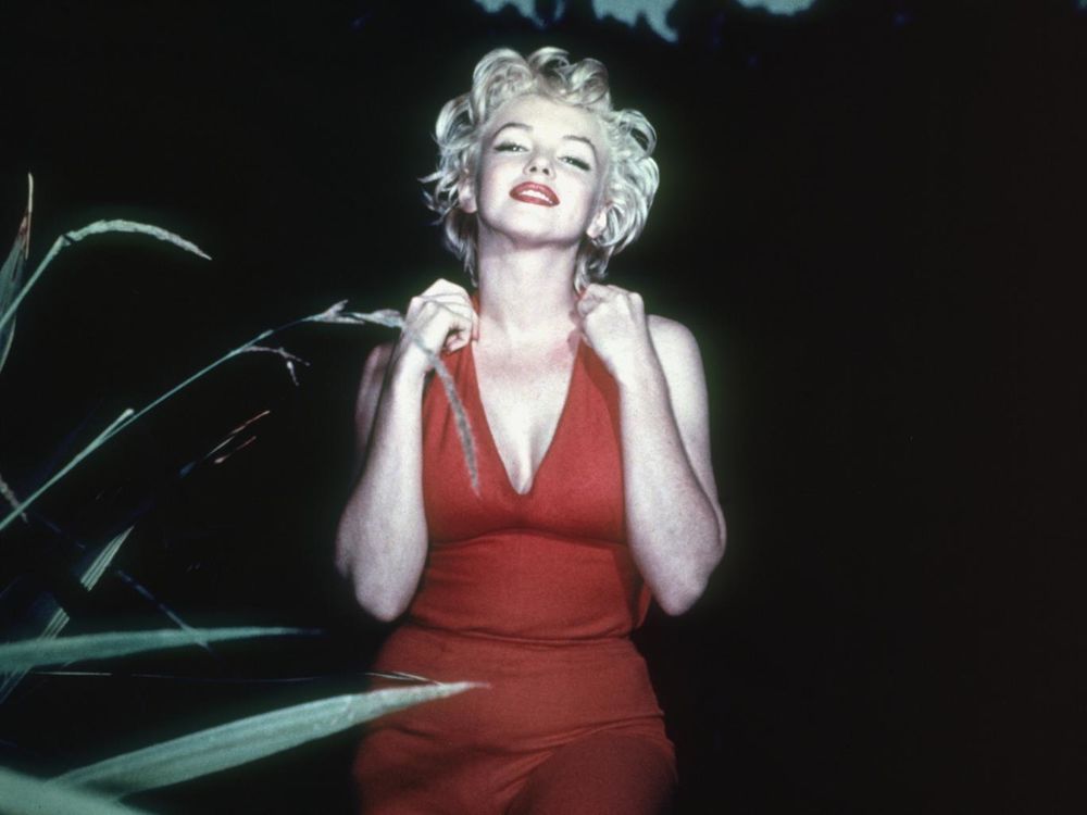 Обои для рабочего стола Marilyn Monroe / Мерилин Монро в красном открытом платье стоит на фоне черного неба