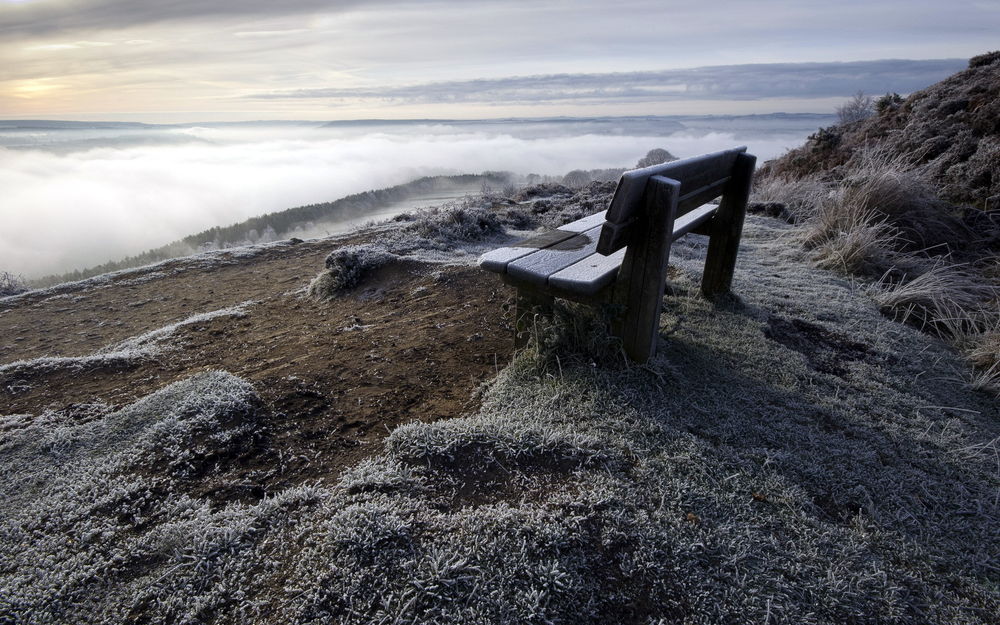 Обои для рабочего стола Одинокая скамейка на склоне горы над облаками и туманами покрытая изморозью