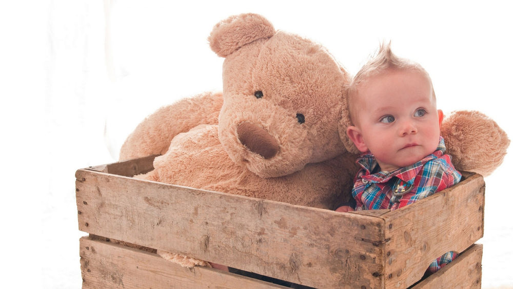Обои для рабочего стола Маленький мальчик с игрушечным медведем в деревянном ящике на белом фоне