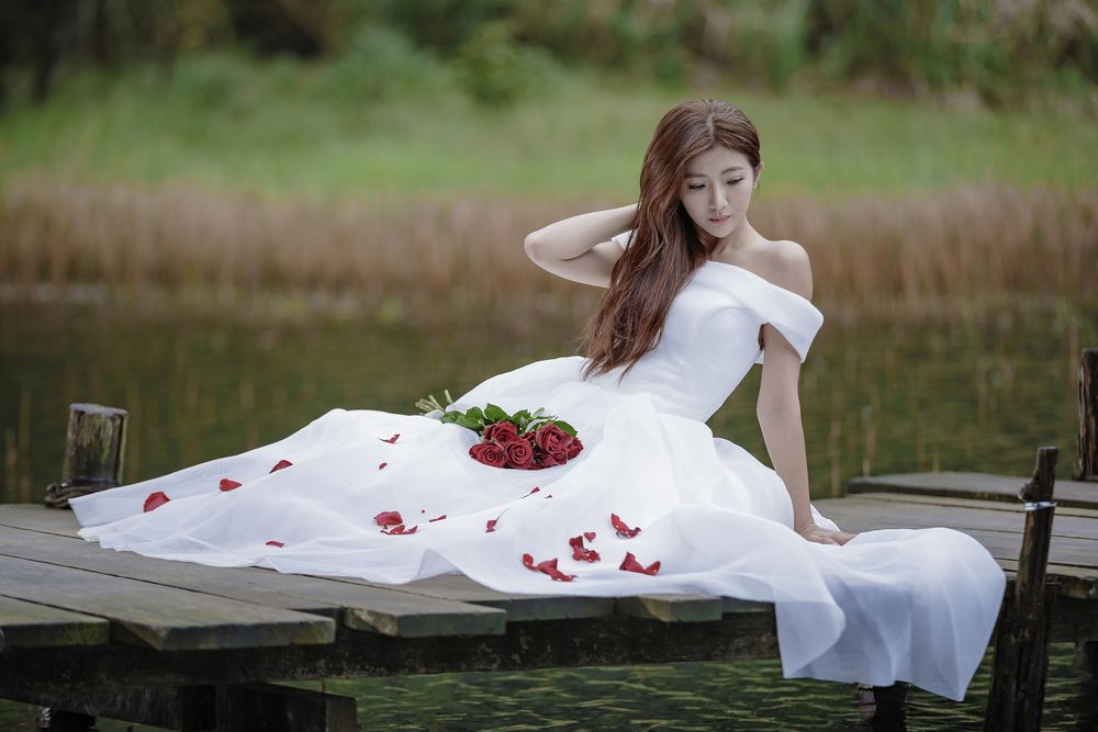 Обои для рабочего стола Азиатка в свадебном платье с букетом сидит на деревянном мостике у пруда
