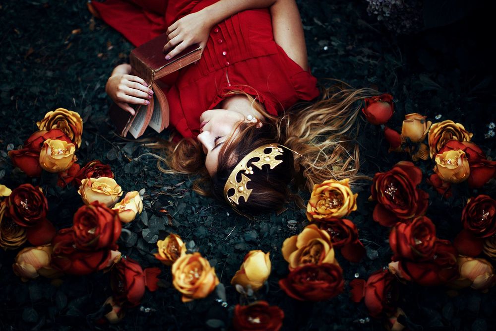 Обои для рабочего стола Девушка с короной на голове и книгой в руках лежит среди роз, фотограф Ronny Garcia