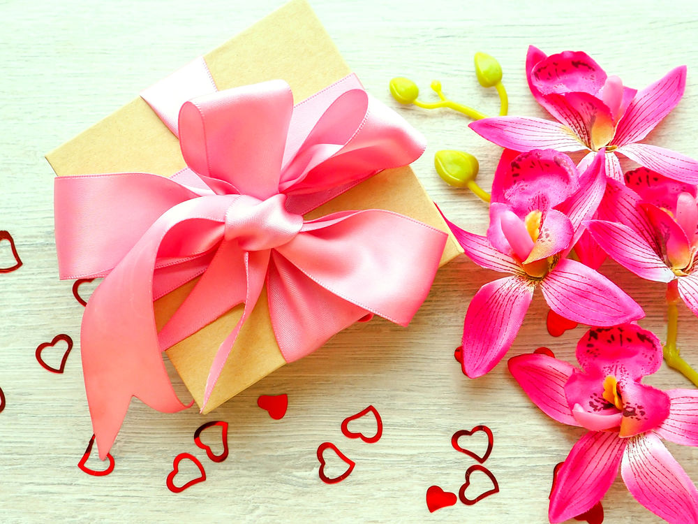 Обои для рабочего стола Коробка с подарком перевязана розовой лентой, рядом сердечки и ветка искусственной орхидеи