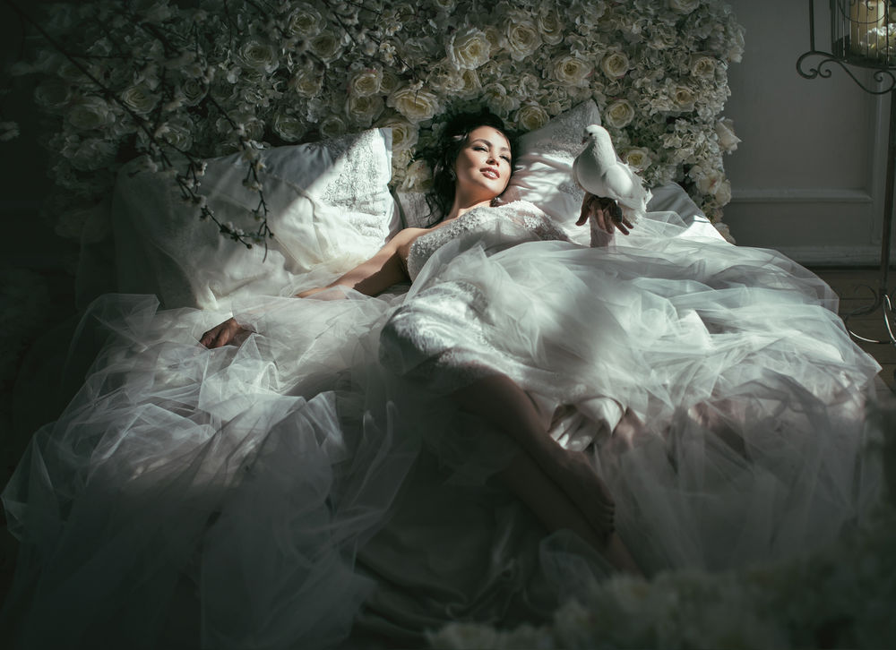 Обои для рабочего стола Красивая, улыбающаяся девушка брюнетка лежит на постели в розах, держа на руке голубя, освещенная лучами солнца, фотограф Валерия Мытник
