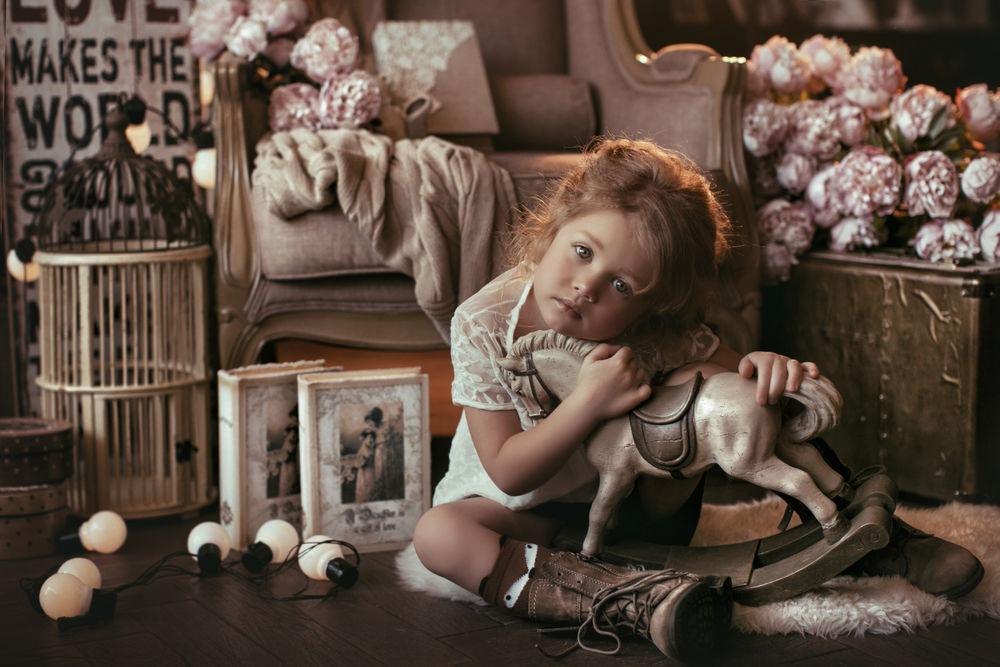 Обои для рабочего стола Грустная маленькая девочка сидит на меховом коврике, обняв деревянную лошадку, фотограф Валерия Мытник