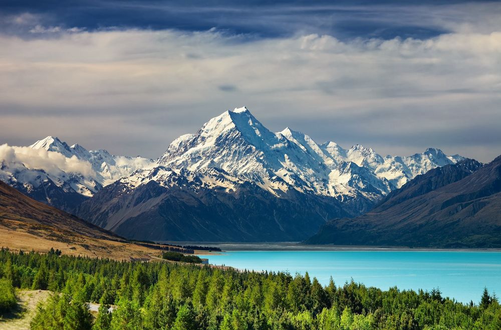 Обои для рабочего стола Озеро Пукаки / Lake Pukaki на острове Южный / South Island в Новой Зеландии / New Zealand на фоне горы Кука / Mount Cook, лесов и облачного неба