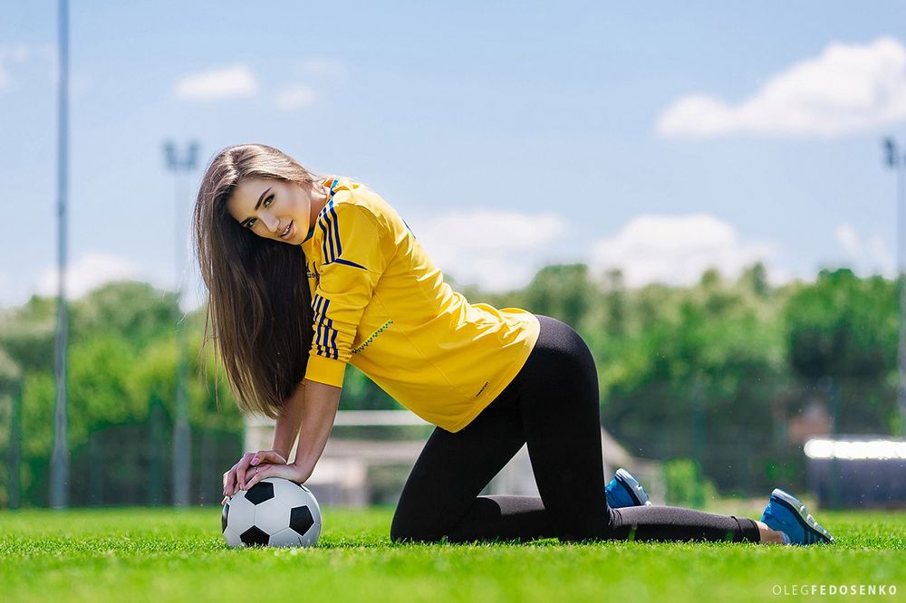 Обои для рабочего стола Модель Настя в футбольной форме стоит на коленях на траве, руки положив на мяч. Фотограф Олег Федосенко