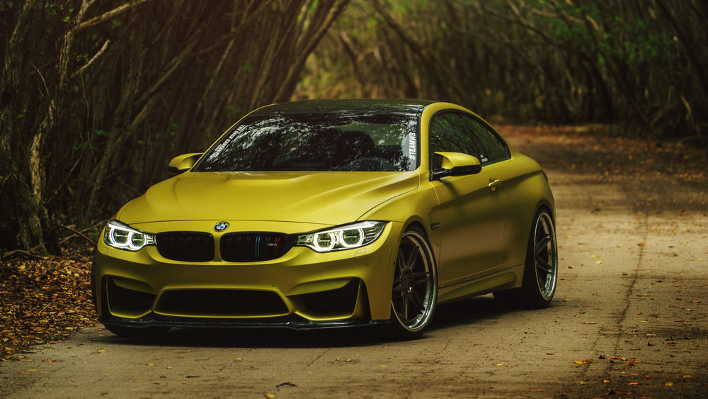 Обои для рабочего стола Автомобиль BMW M4 Coupe Austin Yellow стоит на дороге в тоннеле из деревьев