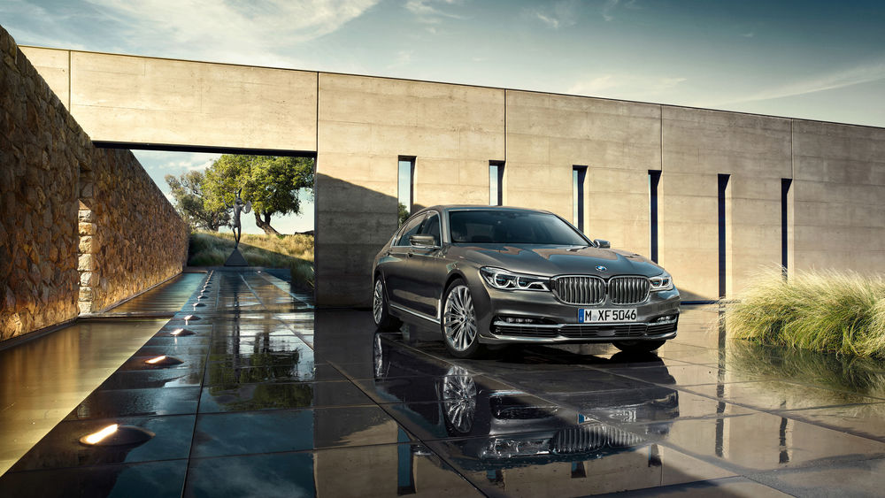 Обои для рабочего стола Автомобиль BMW 750Li xDrive припаркован возле стен с загадочной статуей и деревьями на заднем плане