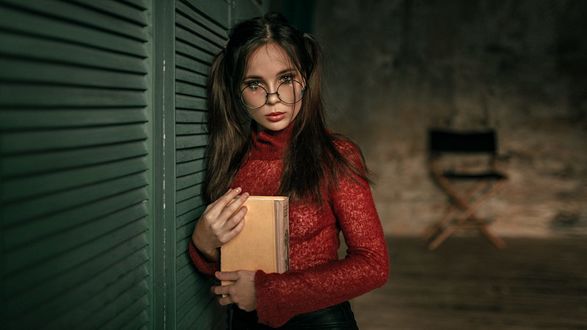 Обои на рабочий стол Девушка в очках, с книгой в руках стоит у стены, фотограф Георгий Чернядьев