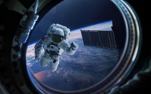Обои на рабочий стол Космонавт в открытом космосе машет рукой через иллюминатор на фоне земли