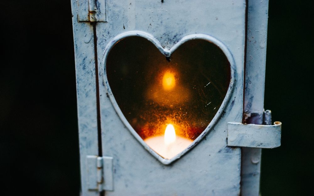 Обои для рабочего стола Отверстие в двери в форме сердца, сквозь него виднеется размытое пламя свечи