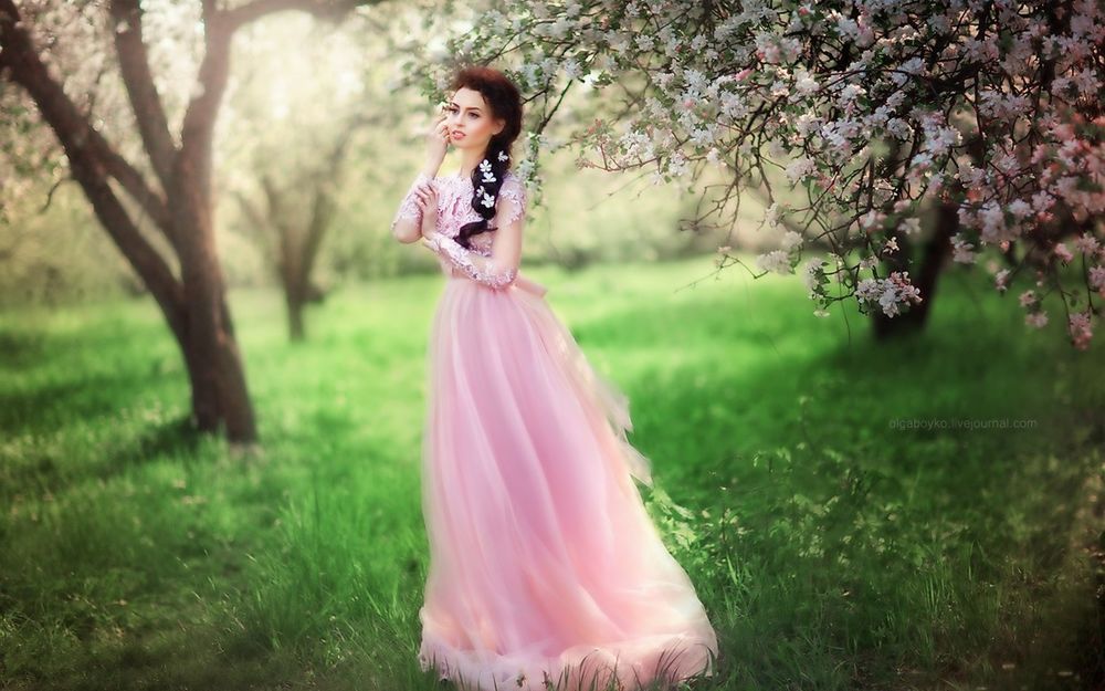 Обои для рабочего стола Девушка в длинном, розовом платье стоит у цветущего дерева в саду