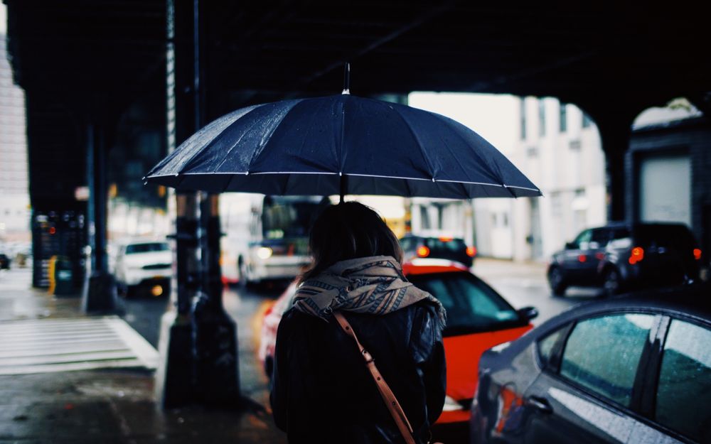 Обои для рабочего стола Девушка под зонтиком стоит спиной на фоне города, затянутого дождем
