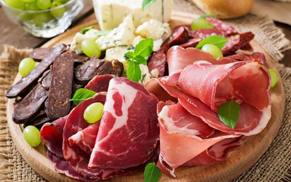 Обои для рабочего стола Аппетитная мясная нарезка и кусочки сыра, украшенные листочками и ягодами винограда на деревянном подносе