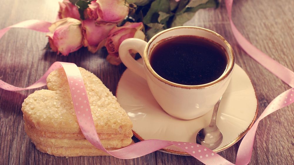Обои для рабочего стола Чашка чая на столе, рядом лежит пирожное в виде сердца и лежат розовые розы