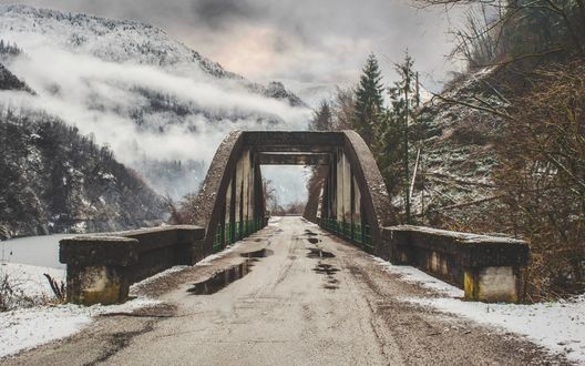 Обои на рабочий стол Мост на дороге, ведущей в заснеженные горы, которые затягивает туманом