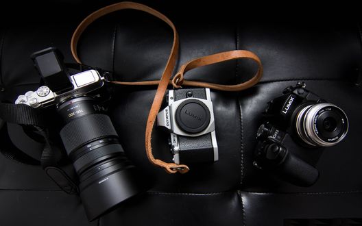 Обои на рабочий стол Фотоаппараты марки Sony, Lens и Olympus лежат на диване
