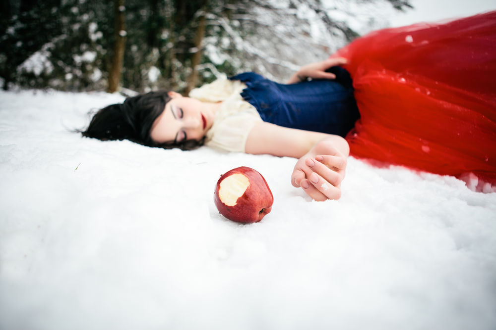 Обои для рабочего стола Девушка в образе Белоснежки лежит на снегу у леса, рядом с ней лежит надкусанное яблоко