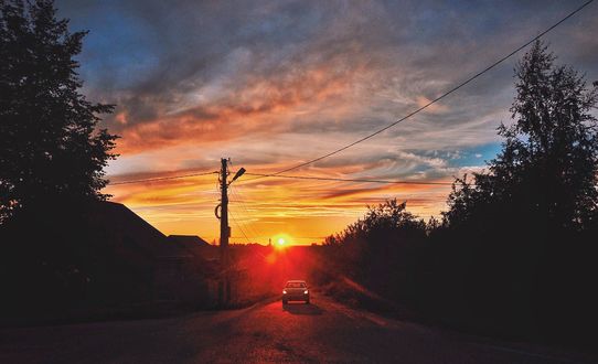 Обои на рабочий стол Автомобиль едет по дороге на фоне заката