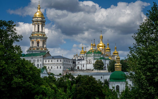 Обои на рабочий стол Комплекс Киево-Печерской Лавры, Киев, Украина виднеется за деревьями на фоне ярко-голубого неба с бело-серыми тучами