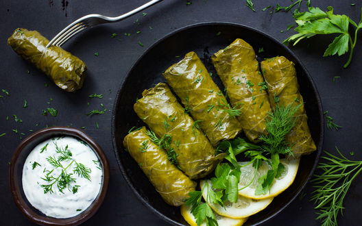 Обои на рабочий стол Долма, украшенная зеленью и кусочками лимона, стоит в сковородке на столе, рядом мисочка сметаны с зеленью