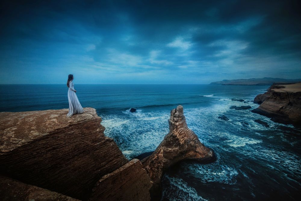 Обои для рабочего стола Девушка стоит на обрыве на фоне волнующегося моря, фотограф TJ Drysdale