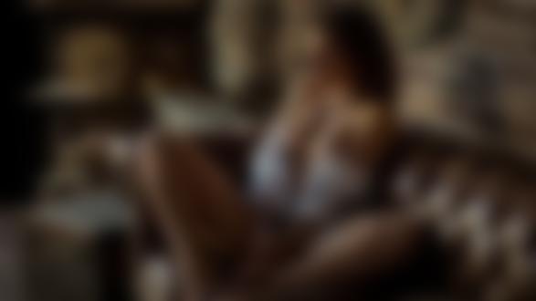 Обои для рабочего стола Девушка в расстегнутой рубашке с красивой грудью сидит в кожаном кресле на фоне кирпичной стены с часами