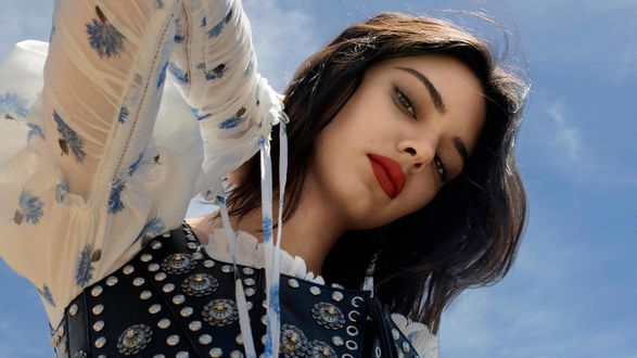 Обои на рабочий стол Американская модель Кендалл Николь Дженнер / Kendall Nicole Jenner подняла вверх руку на фоне голубого неба