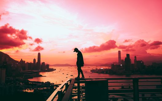 Обои на рабочий стол Мужчина стоит на мостках над водоемом на фоне города и розового закатного неба, фотограф Anthony Intraversato