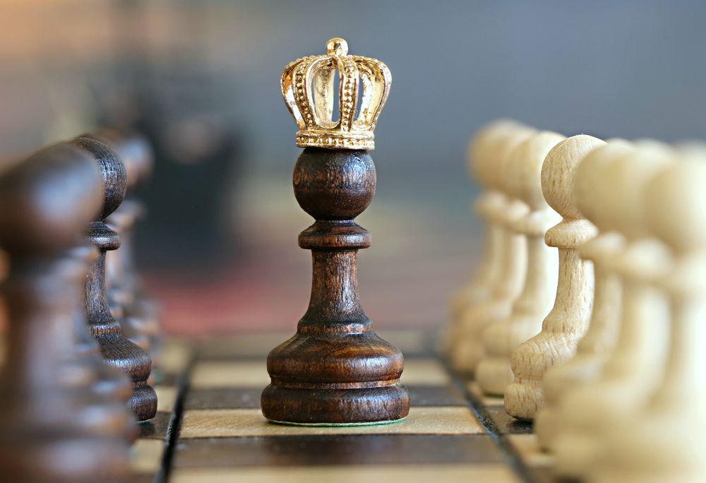 Обои для рабочего стола Черная пешка в короне стоит на шахматной доске на размытом фоне