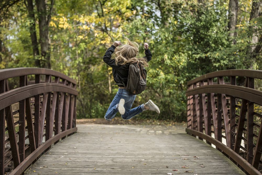 Обои для рабочего стола Девушка с рюкзаком за спиной в прыжке на фоне природы, на мосту, фотограф Себастьян Воортман