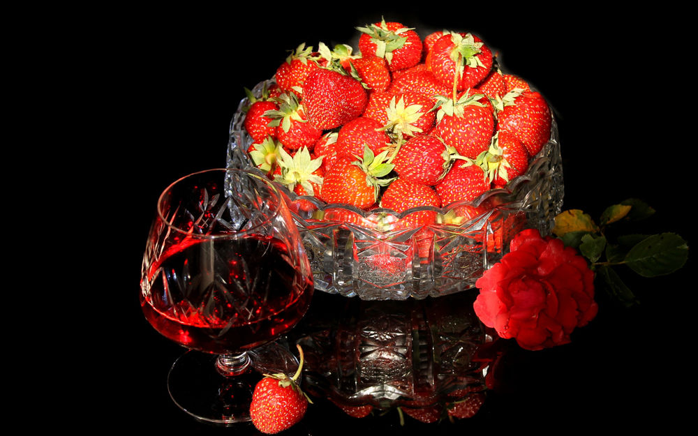 Обои для рабочего стола Бокал клубничного ликера и блюдо спелой клубники рядом с красной розой на черном фоне