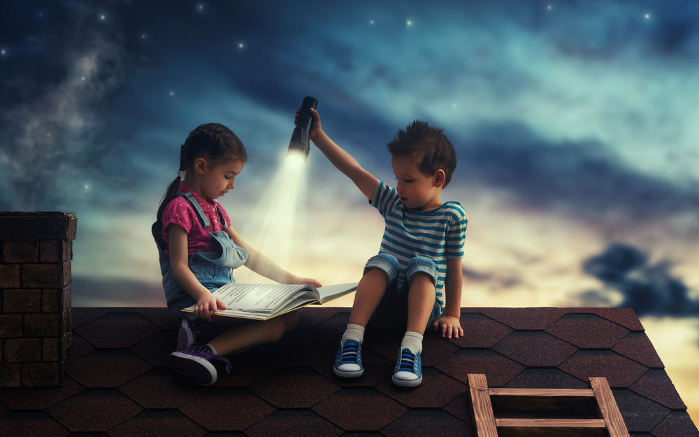 Обои для рабочего стола Двое детей на крыше читают книгу ночью при свете фонаря