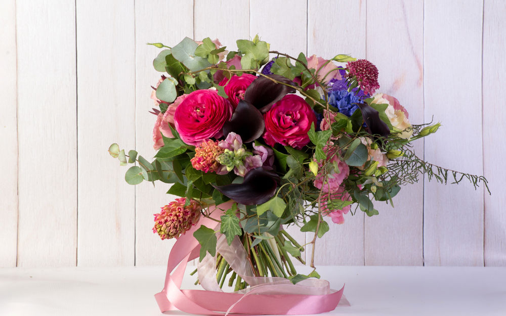 Обои для рабочего стола Праздничный букет цветов стоит на столе, перевитый розовыми лентами