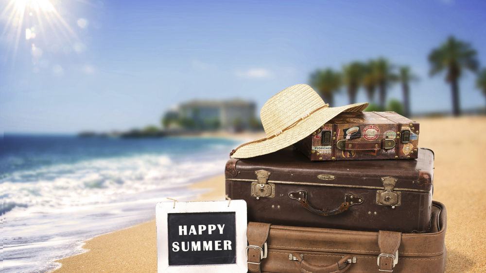 Обои для рабочего стола Стопка чемоданов на берегу моря, сверху лежит шляпа, рядом табличка Happy summer / Счастливого лета