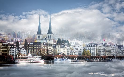 Обои на рабочий стол Zurich / Цюрих в облаках со шпилями храма и домами возле реки, Швейцария / Switzerland