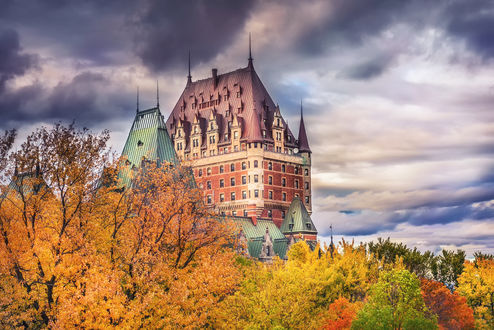 Обои на рабочий стол Отель Quebec, Kanada / Квебек, Канада среди осенних деревьев с желтыми, красными и зелеными листьями на фоне неба с облаками