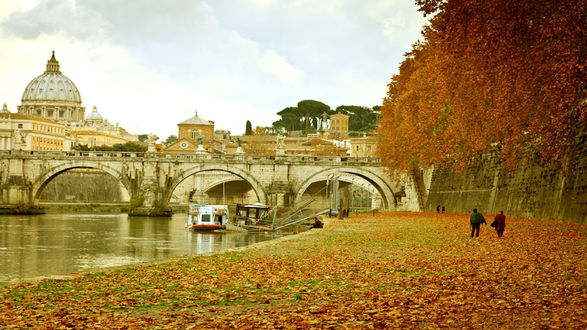Обои на рабочий стол Rome, Italy / Рим, Италия) осенью. Берег реки с мостом, усыпанный желтыми листьями с деревьев, по реке плывет корабль, на берегу гуляют люди, вдалеке виден Собор Святого Петра