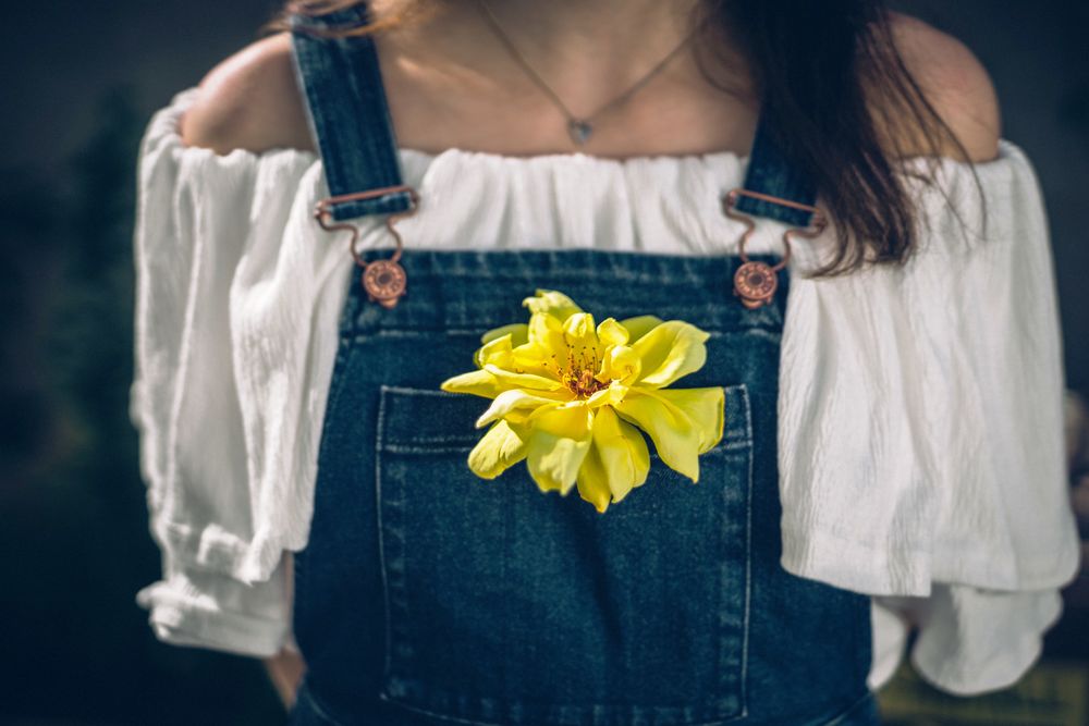 Обои для рабочего стола Девушка в кофточке и джинсовом комбинезоне, в карман которого вставлен желтый цветок